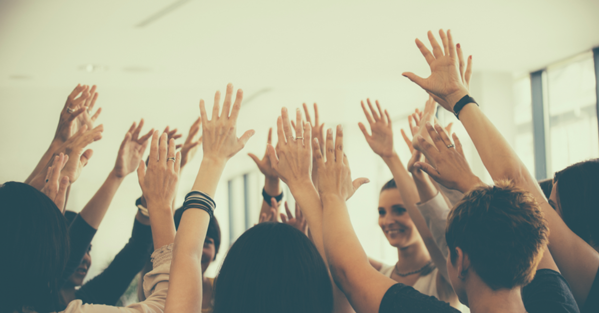 Employees in a circle raising hands. 
